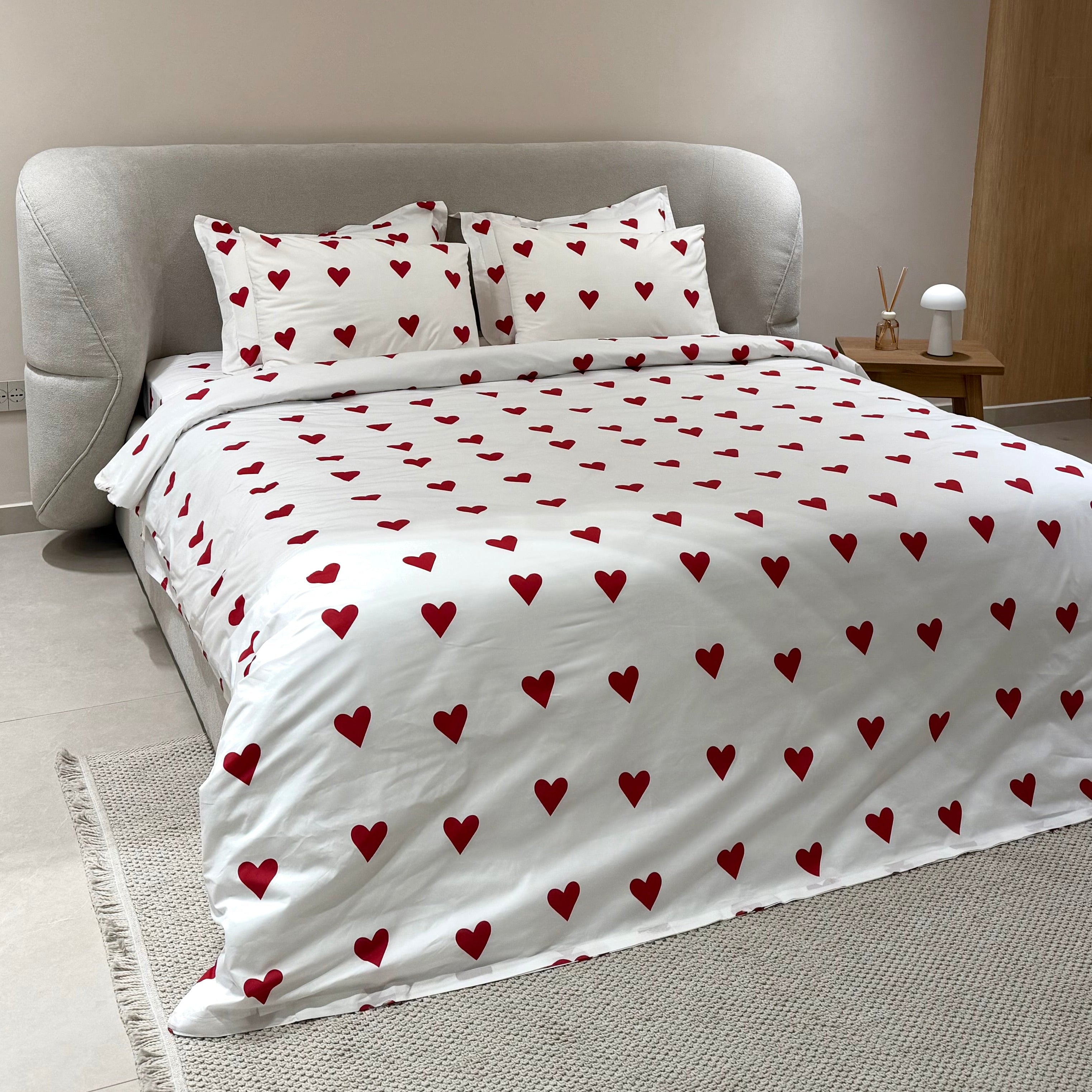 Bed with red heart pattern bedding and matching pillows in a bedroom setting.