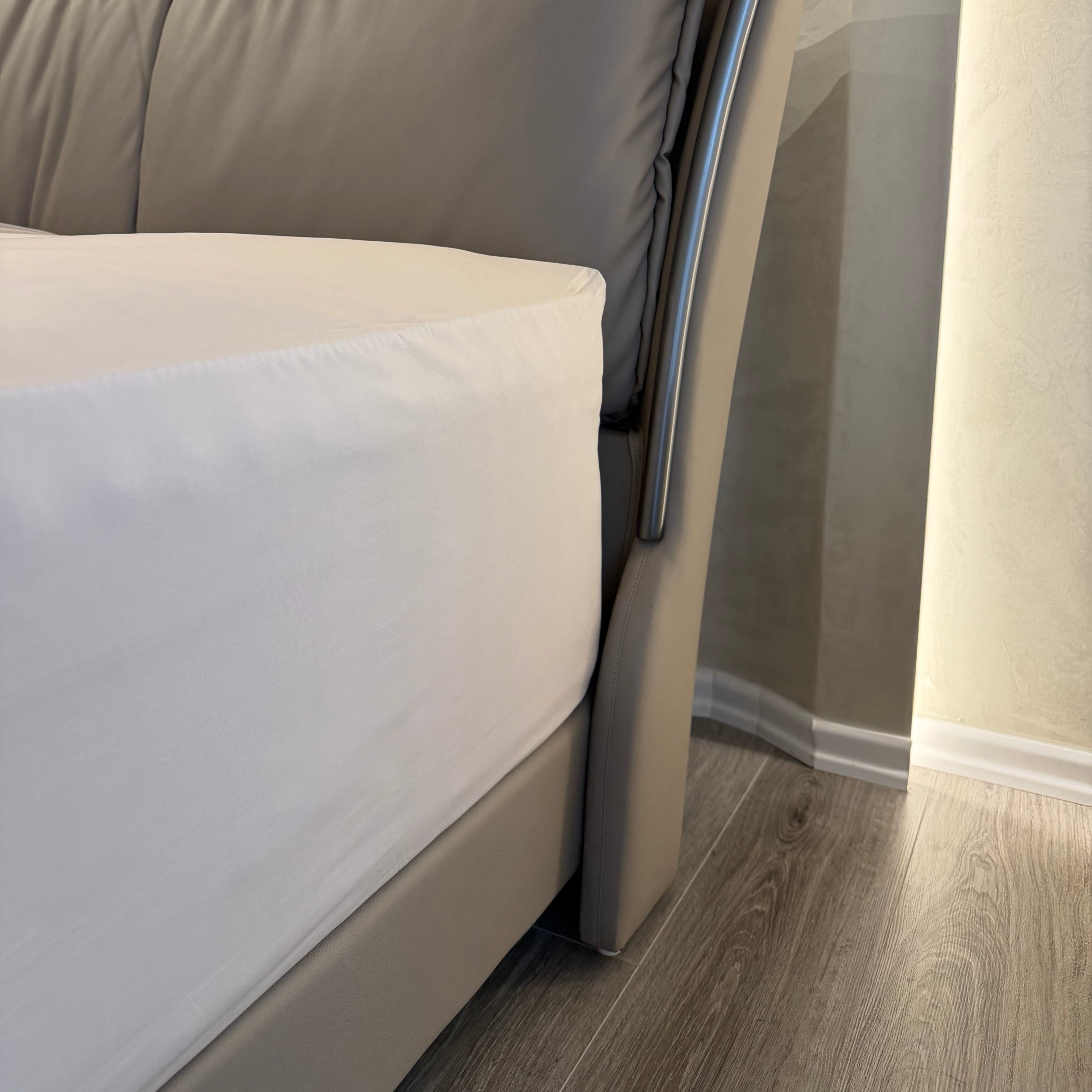 Close-up of a bed with beige pillows and a white mattress against a neutral wall.