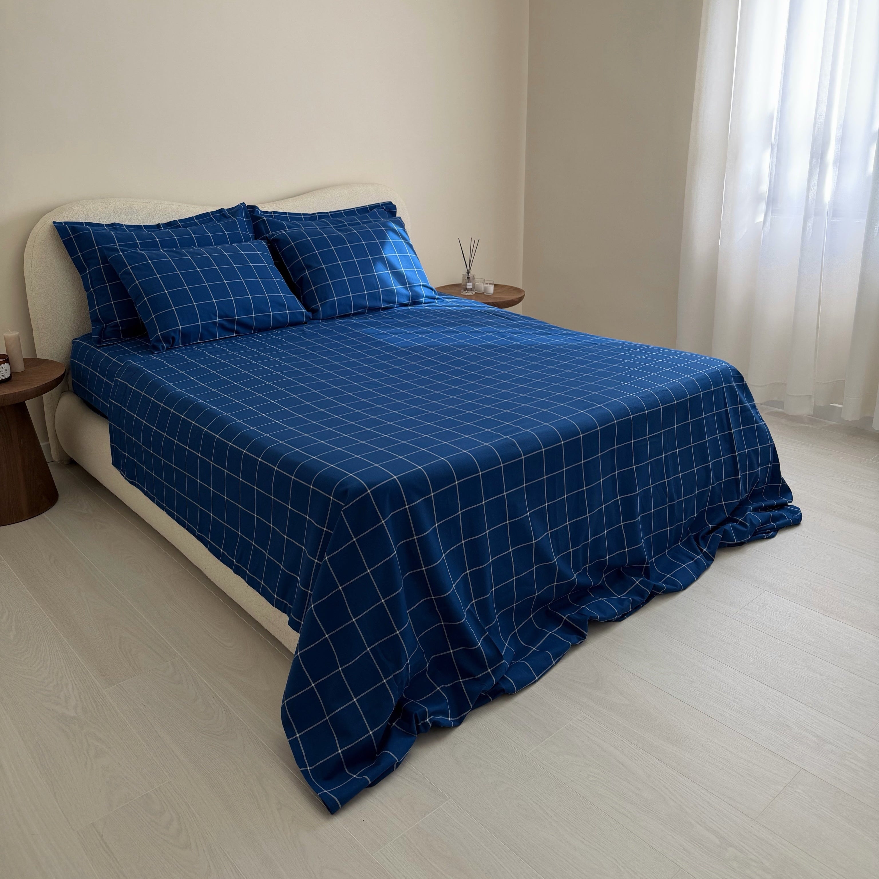 Bed with blue checkered bedding in a room with white walls and curtains.
