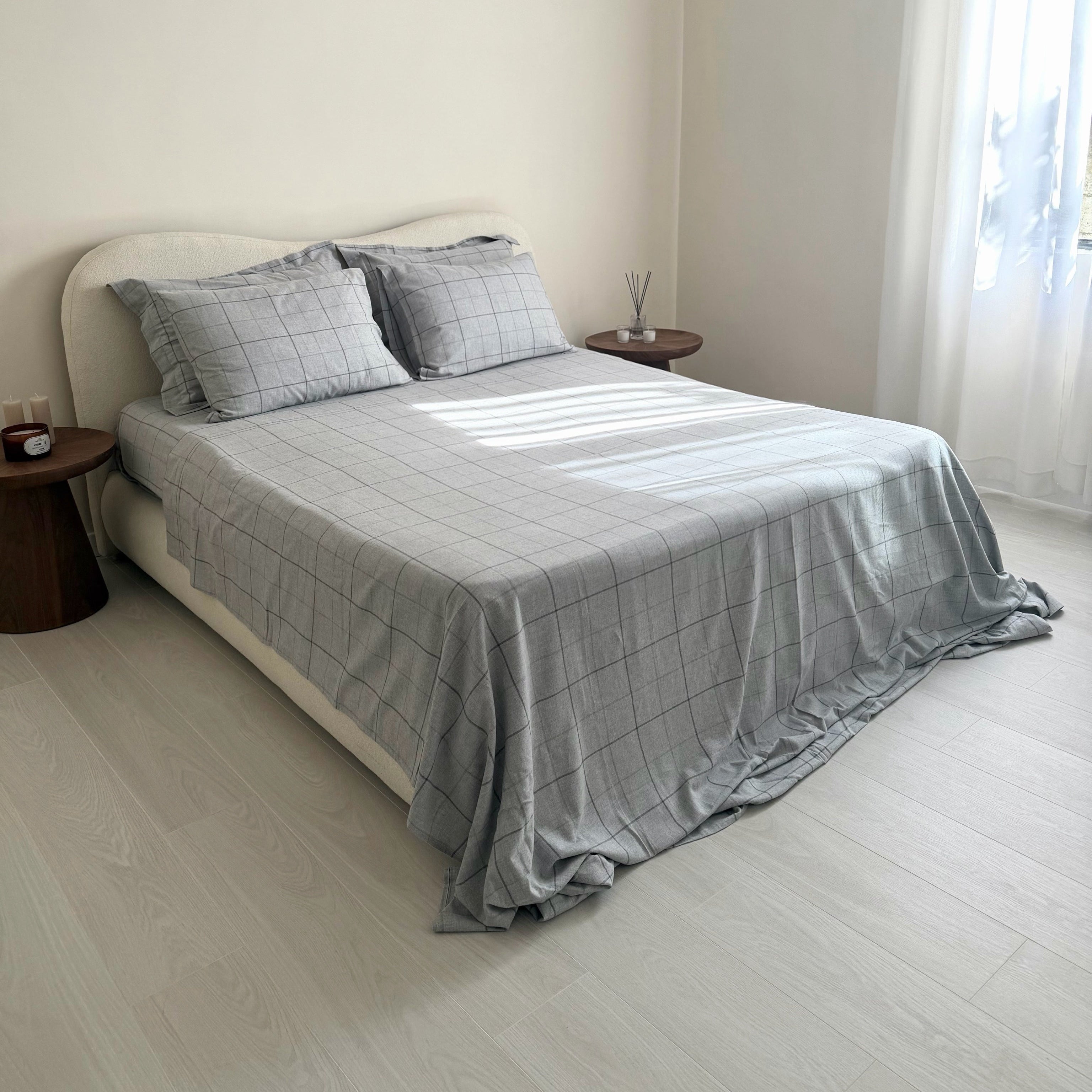 Bedroom with a bed covered in gray bedding and pillows, next to a window with white curtains.