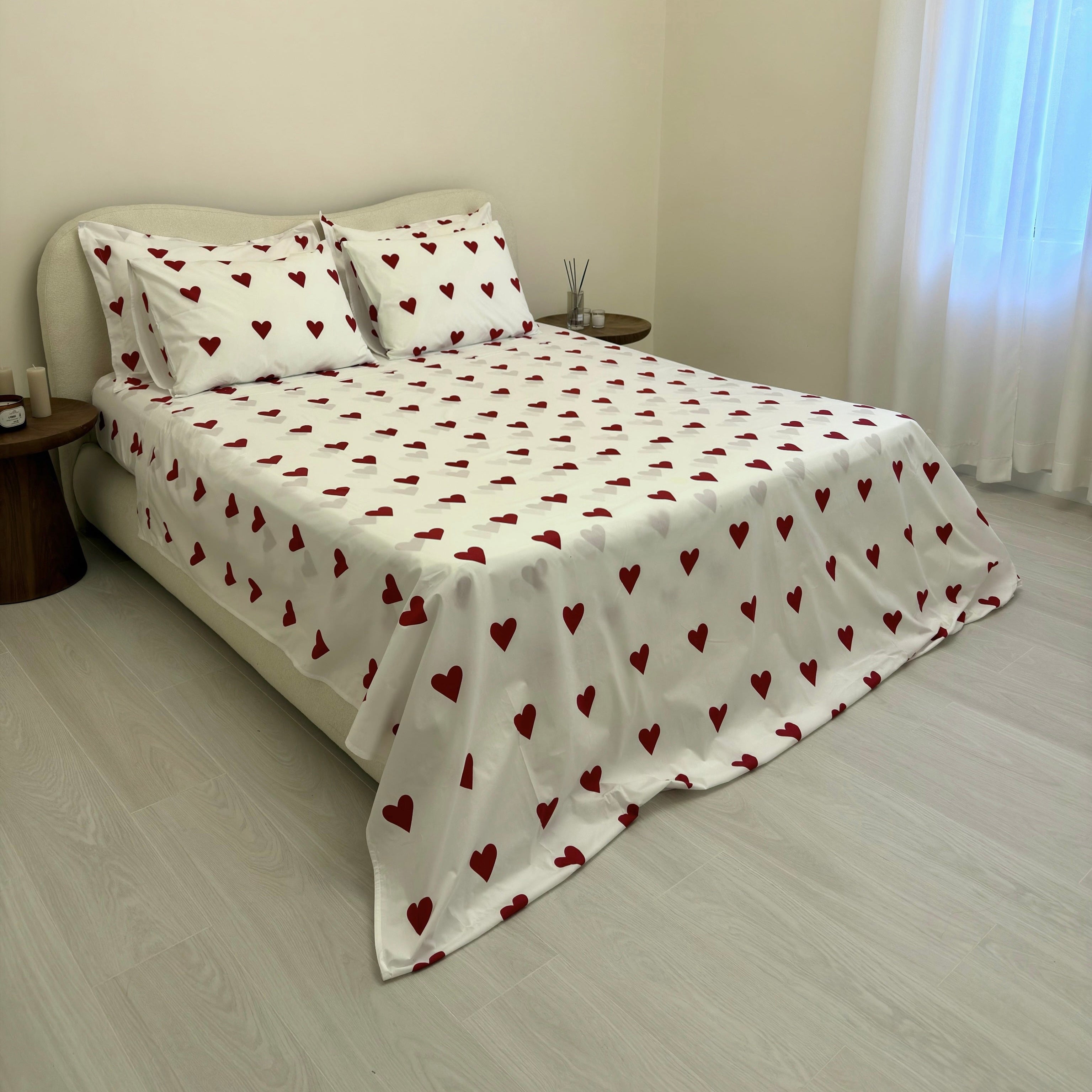 Bed with heart-patterned bedding in a room with a curtain.