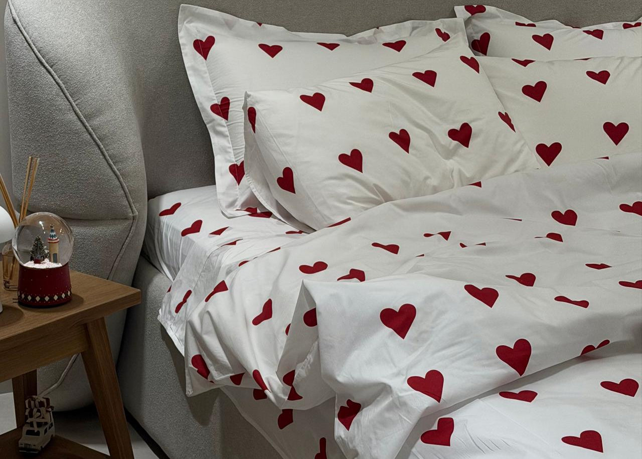 Bed with white bedding and red heart patterns, next to a wooden side table.